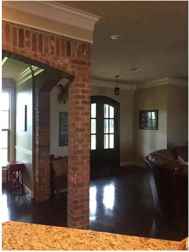 Entry hall seen through a brick arch, with an arched wood front door and crown molding