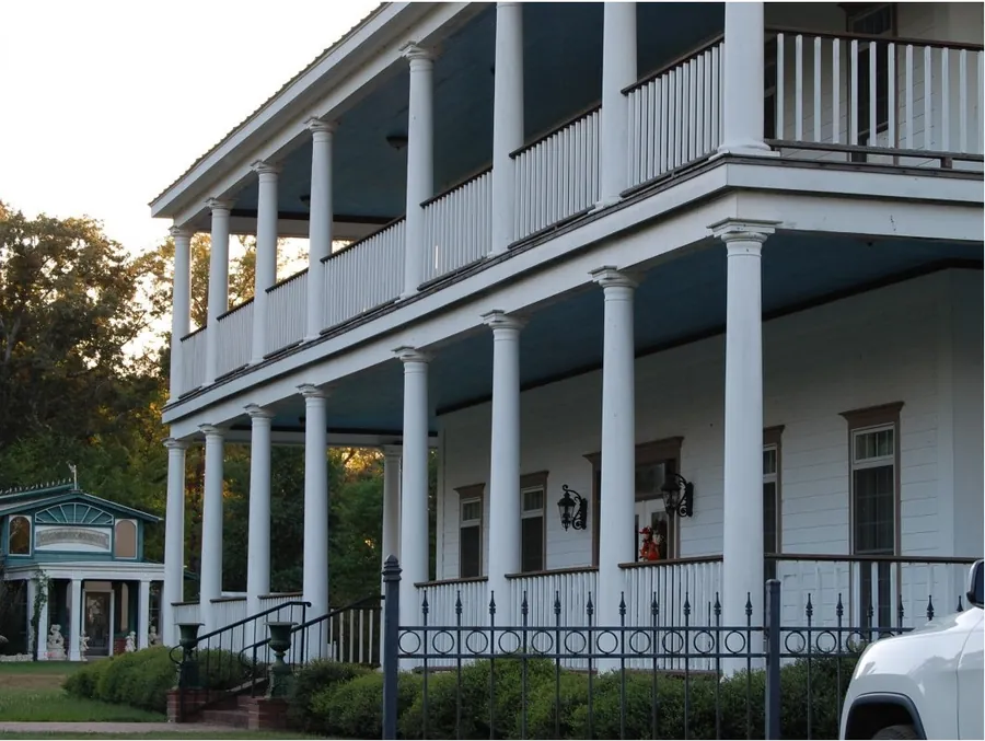White two-story home with tall round columns, a blue porch ceiling and an iron fence