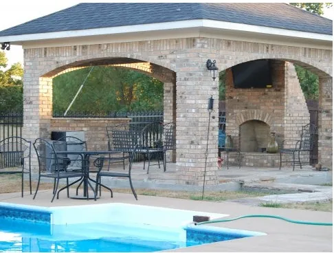 Brick poolside pavilion with arched openings, an outdoor fireplace and a mounted TV